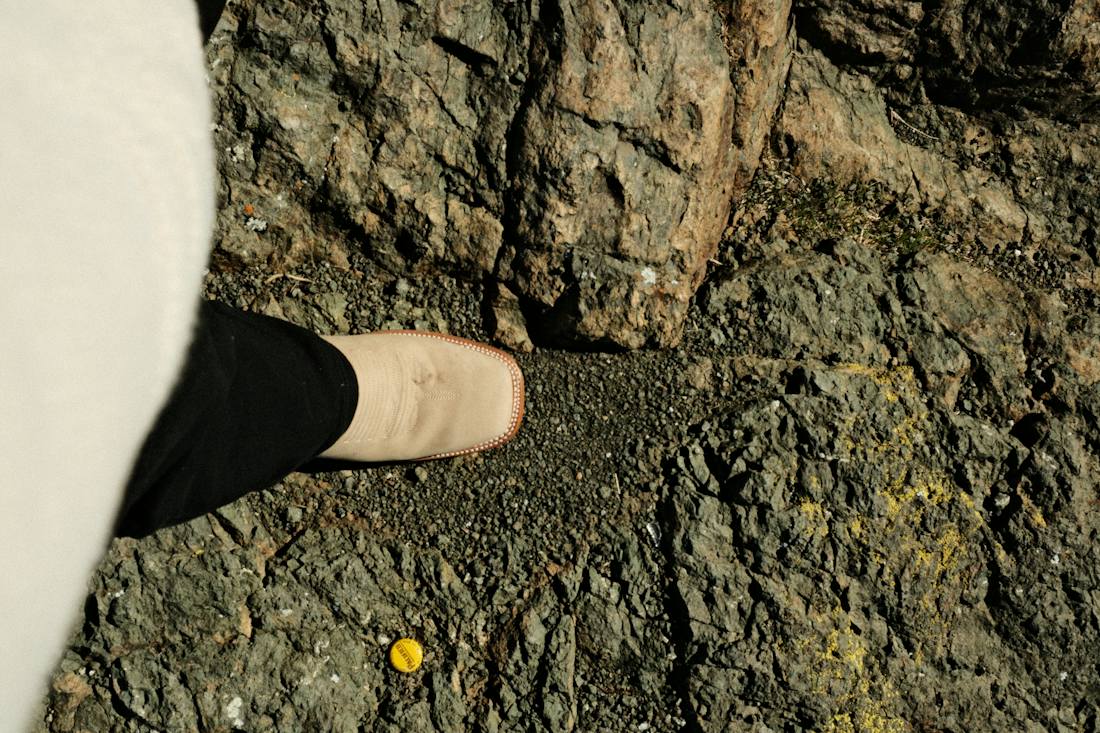 A foot in a light walking shoe stepping onto a gravel path beside a rough rock face