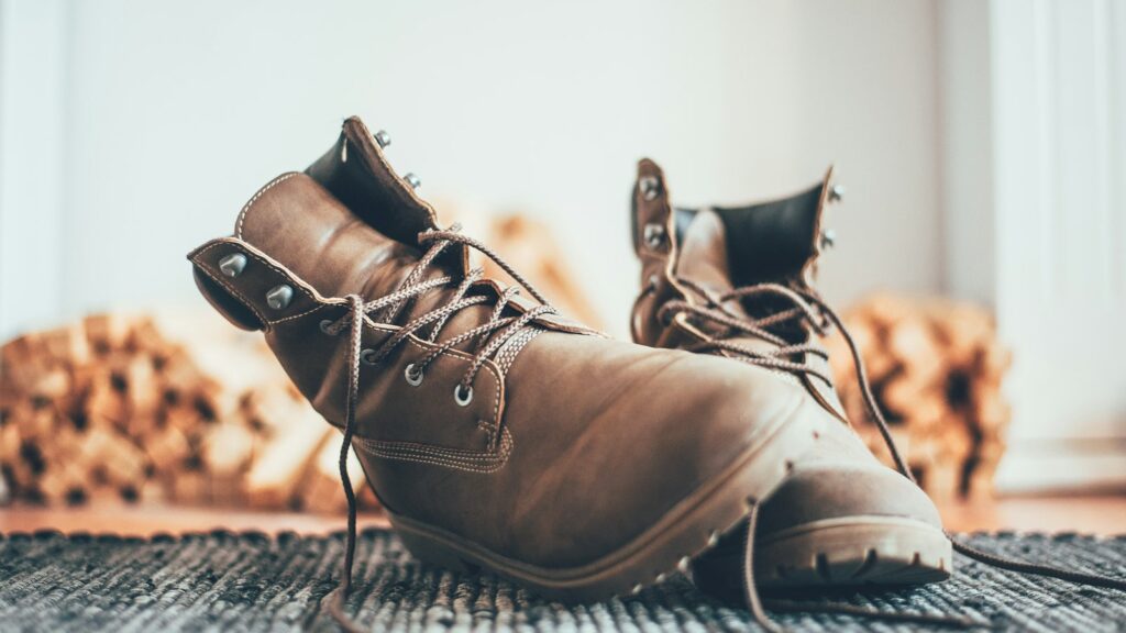 A pair of worn brown leather lace-up boots resting on a woven rug in soft daylight