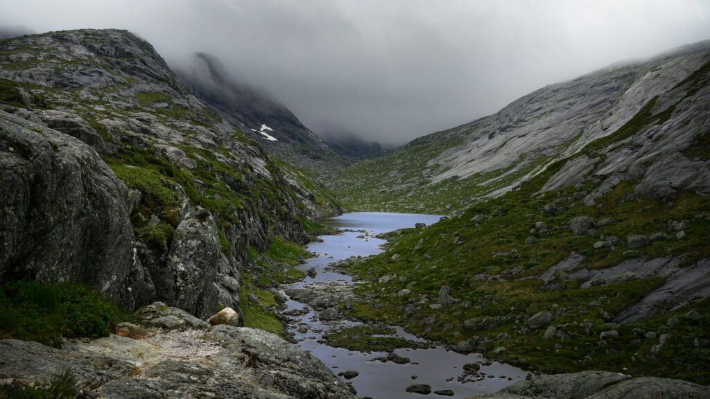A rocky Nordic valley with a small lake and a stream beneath low grey clouds