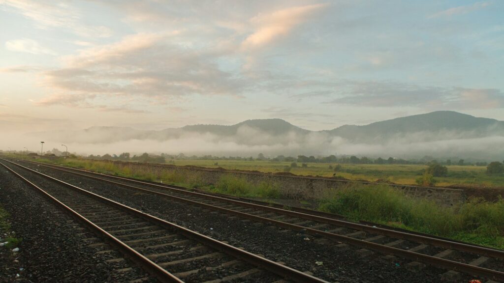 Railway tracks running towards low hills wrapped in morning mist under a soft pastel sky