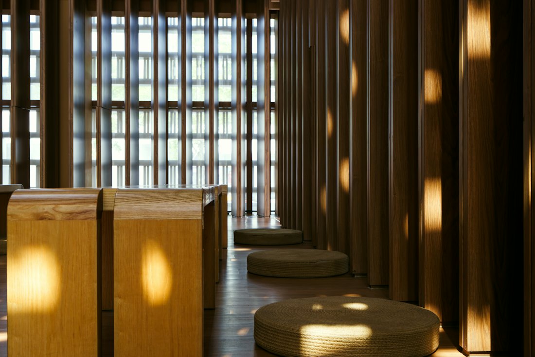 Round woven floor cushions in a calm wooden hall with sunlight falling through tall slatted windows