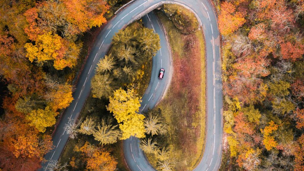 An aerial view of a hairpin road winding through a forest of orange and gold autumn trees